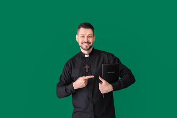 Handsome priest with Bible on color background