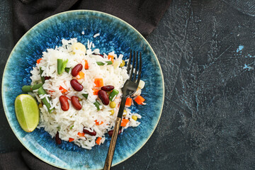 Plate with tasty rice, beans and vegetables on dark background