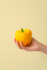 Female hand with yellow bell pepper on color background