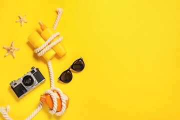 Bottles of sunscreen with sunglasses and photo camera on color background