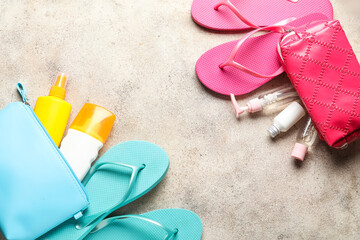 Bags with sunscreen cream and flip-flops on grey background