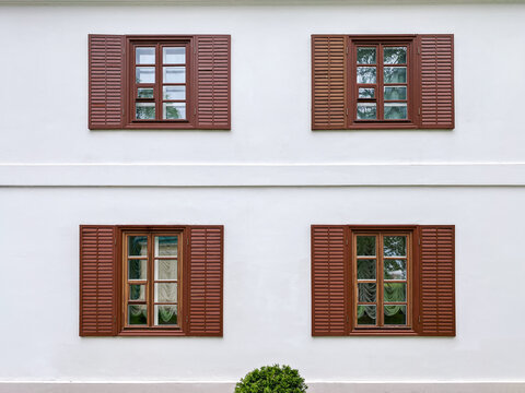 white exterior plaster wall with painted brown windows and wooden shutters
