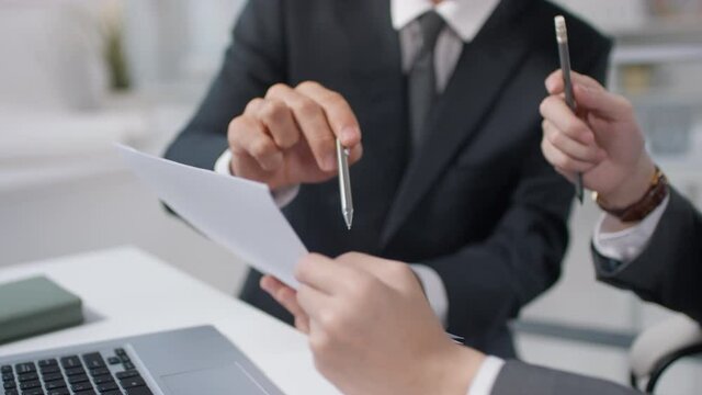 Two unrecognizable men wearing suits sitting at office desk working together on business plan strategy using pen and papers