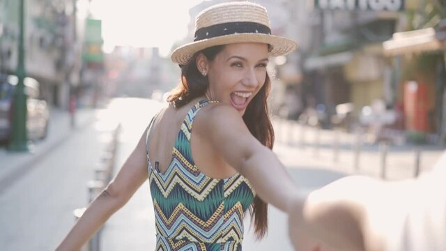 Slow motion of young brunette stylish woman holding hands with beautiful toothy smile. Romantic Hispanic girl friend taking boyfriend together for adventure journey. Dating and honeymoon travel
