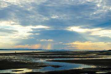 Obraz premium Sunset over Moreton Bay, with light streaming down from behind grey clouds, and people walking to King Island at low tide. Wellington Point.