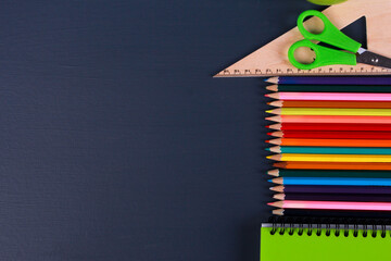 Colorful pencils, green notebook, scissors, ruler on dark blue background. Top view, copy space,...