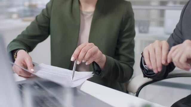Two modern business partners sitting together at office desk working on business agreement, headless handheld shot