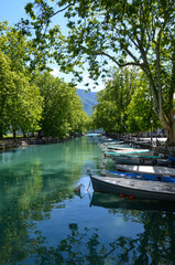 Alpine town Annecy in Upper Savoy, France, colorful boats on river Thiou, trees on both sides of the riverbanks, a sunny day in summer