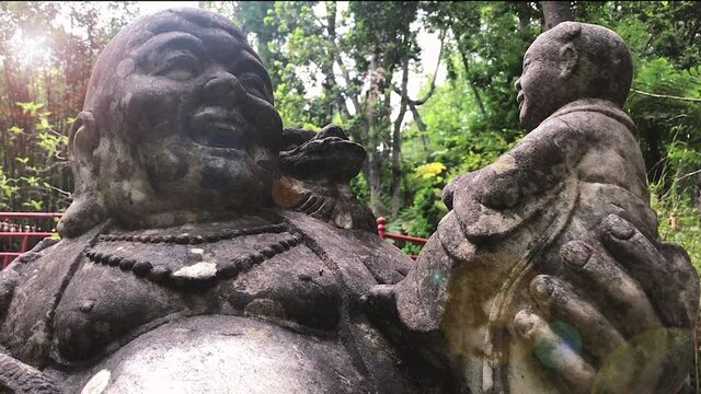 Laughing Buddha statue holding baby in oriental garden setting. Handheld. Circle pan.