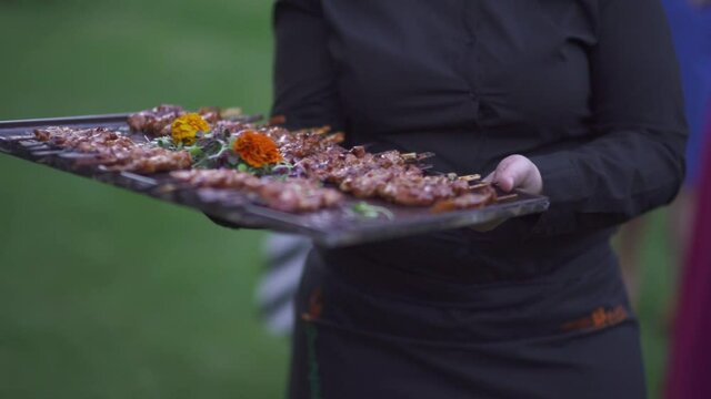 Female server in black outfit offering meat skewers to event's guests