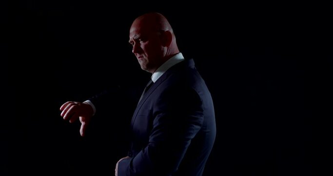 the bald man is dressed in a dark business suit. he slowly rotates on a black background and shows disapproval, thumbs down, aversion, rejection gesture, thumbs up