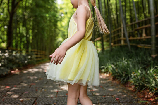 Cute little girl in yellow tutu dress dancing in bamboo forest in China. Kid with blonde hair from behind outdoor
