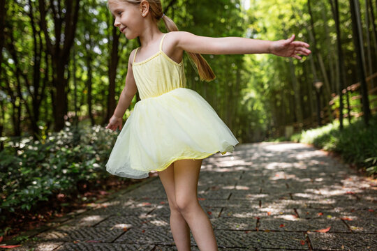 Cute little girl in yellow tutu dress dancing in bamboo forest in China. Kid with blonde hair from behind outdoor