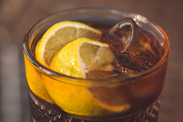 Glass of Long Island iced tea with lemon slice and straw. Close-up of an amber-colored alcoholic drink with ice on table in a bar, cafe. - Powered by Adobe