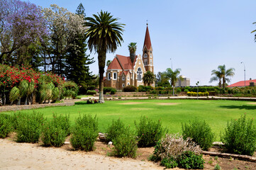 Beautiful Lutheran Christ Church (Christuskirche) in the public park with Jacaranda tree, Palms and green lawn in Windhoek, Namibia