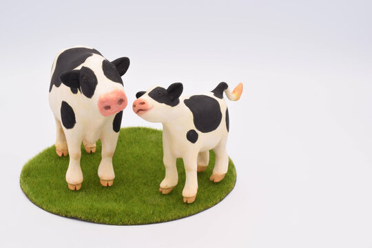 寄り添う牛の親子の粘土人形　足下に芝生の背景イメージ