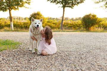Pretty little girl with a big white dog in the park. A beautiful 7 year old girl in pink dress hugs her favorite dog during a summer walk.