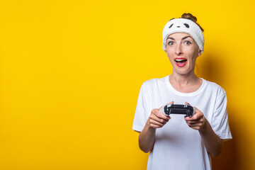 Young woman with a kindred expression with a joystick in hands on a yellow background.
