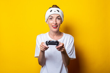 Young woman plays a virtual game with a joystick in her hands on a yellow background.