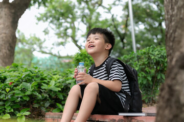 Cute little boy drinking mineral water from the plastic bottle in the park