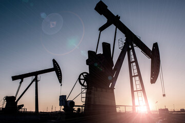 Oil pumps are running in the sunset at the oil field.