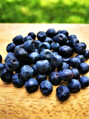 Blueberry (Vaccinium myrtillus) close-up. Berries on a wooden board in the background of green grass. Forest fruits.