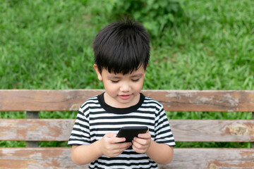 Cute little boy sitting on a park bench and playing with mobile phone