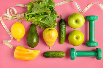 Composition with dumbbells, green and yellow vegetables and fruits, measuring tape on a pink background, top view. The concept of dietary nutrition and a healthy lifestyle.