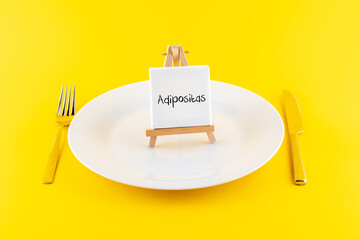 Schild Adipositas auf einem leeren Teller mit Besteck