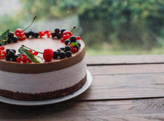 Mousse cake with berries on a wooden table. Chocolate cream cake with currants and cherries. Berry cake for birthday, wedding and other holidays.