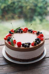 Mousse cake with berries on a wooden table. Chocolate cream cake with currants and cherries. Berry cake for birthday, wedding and other holidays.