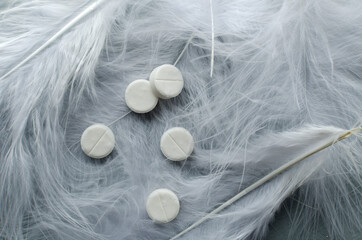 Top view of white round tablets for sleep on the feathers.Empty space