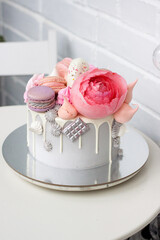 Modern grey cake with pink peony flowers, chocolate and macaroons for a wedding or a celebration. White background.