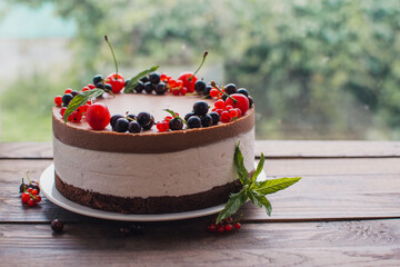 Mousse cake with berries on a wooden table. Chocolate cream cake with currants and cherries. Berry cake for birthday, wedding and other holidays.