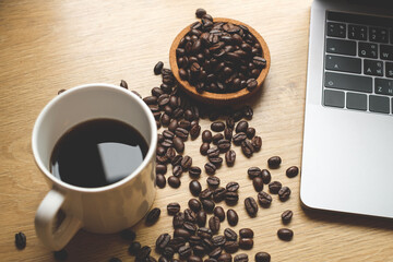 Black coffee with coffee bean and laptop computer on wooden table copy space
