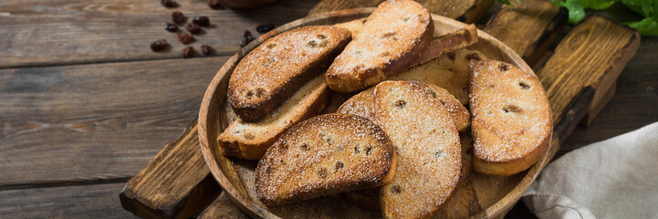 Crackers with sugar and raisins on a wooden plate on a brown wooden table. A lot of crackers in the plate. Rustic style. Banner with space for text