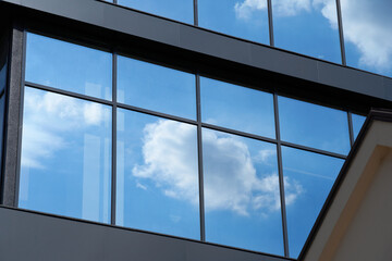 facade of a modern building on a bright Sunny day, blue sky and clouds reflecting in a glass, beautiful exterior of the new building