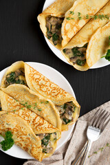 Savory Homemade Mushroom, Spinach and Cheese Crepes on a white plate on a black background, top view. Flat lay, overhead, from above.