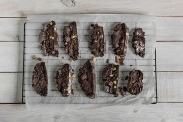 Homemade chocolate biscotti or cantuccini with pistachios on baking paper, top view over a white rustic wooden table.