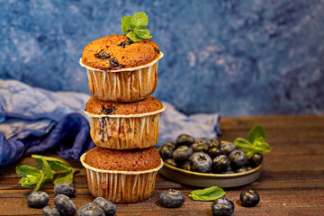 Three fragrant, delicious muffins in the form of a pyramid stand on wooden boards, decorated with blueberries and mint. Horizontal orientation.Backspace.
