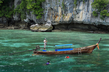 Fototapeta na wymiar Longtailboat with tourists, near eroded overgrown limestone rocks in Phang Nga Bay, Ao Phang Nga Marine National Park, Thailand,