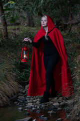 Attractive woman dressed a little red riding-hood cross stream in a dark forest with a lantern - 363478065