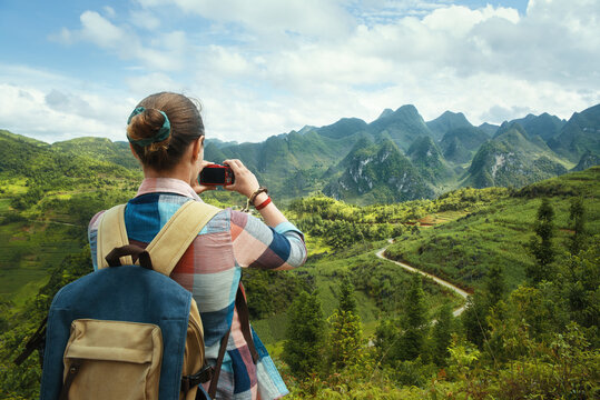 Woman Traveler with backpack, photographs a beautiful view of the karsts mountains in the North of Vietnam. Traveling along mountains, freedom and active lifestyle concept.