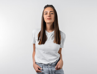 Young carefree modern girl with long chestnut hairs in casual white clothes posing isolated on white wall background. People lifestyle concept.