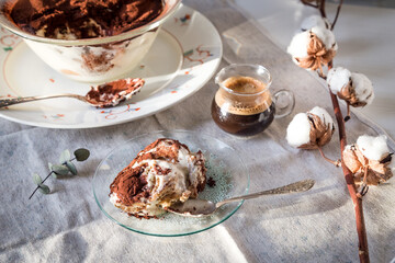 Glass bowl and plate with tiramisu dessert on white kitchen table.