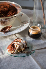 Glass bowl and plate with tiramisu dessert on white kitchen table.