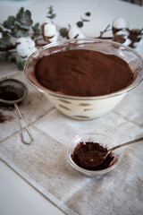 Bowl with homemade tiramisu, cocoa powder and sieve on white background.