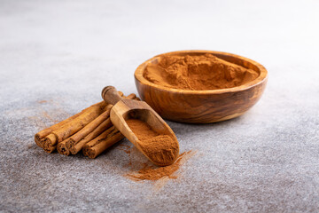 Ceylon cinnamon sticks with cinnamon powder in wooden bowl on concrete background. Copy space.