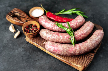 raw sausages with spices and rosemary on a stone background