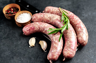 raw sausages on a meat knife with spices and rosemary on a stone background
